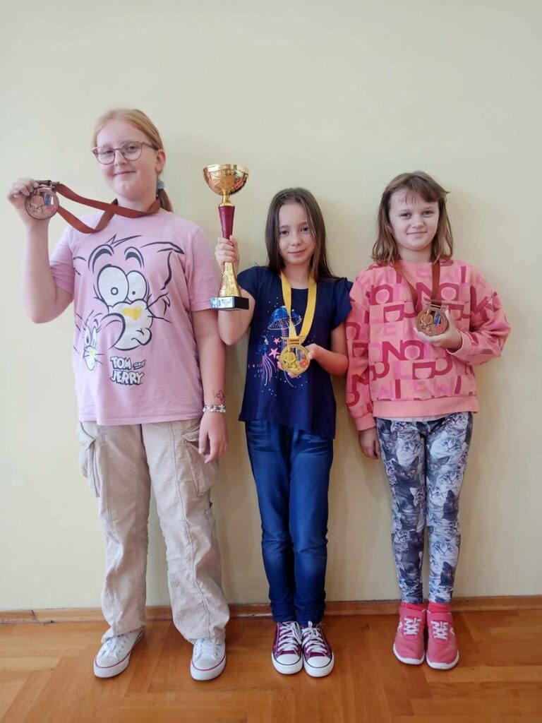 Zdjęcie przedstawia uczennice klasy 4c, pozują one z medalami i pucharem zdobytym na zawodach karate.