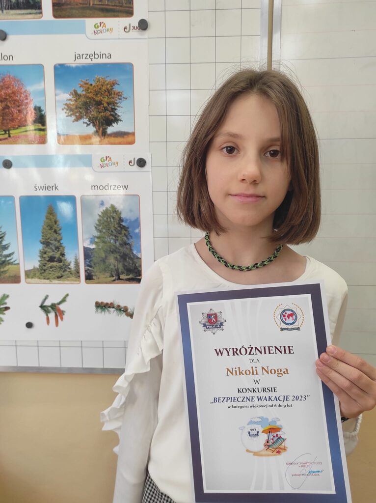Zdjęcie przedstawia Nikolę z klasy 3a, uczennica trzyma przed sobą dyplom - wyróżnienie w konkursie  "bezpieczne wakacje 2023"