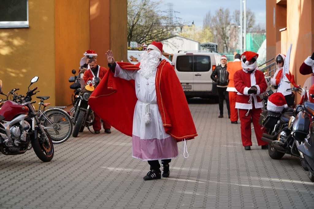 Zdjęcie przedstawia Św. Mikołaja w tradycyjnym czerwonym stroju. Widzimy też motocykle i inne osoby przebrane za  mikołajów.